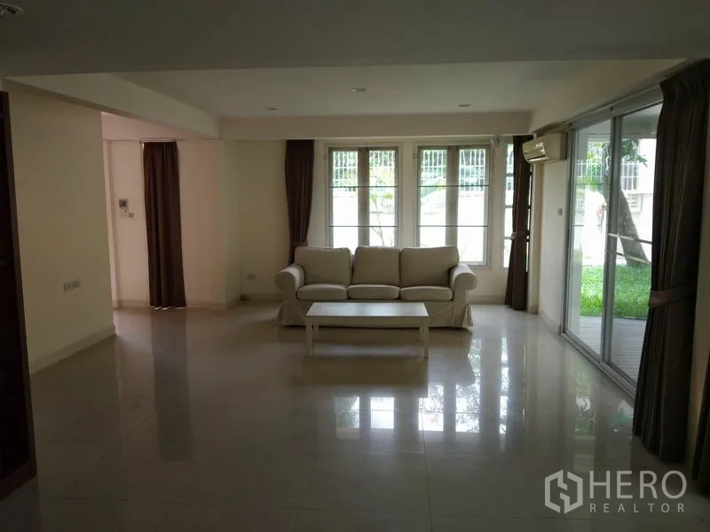 Detached House for rent in Watthana, Bangkok - Spacious living room with sofa and coffee table, sliding doors opening to the garden.