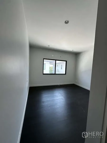 Detached House for sale in Lam Luk Ka, Pathum Thani - Compact bedroom with window and dark wood floor.