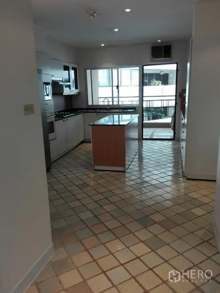 Condominium for rent in Khlong Toei, Bangkok - Bright kitchen with center island, built-in appliances, tiled floor, and a view toward the balcony.