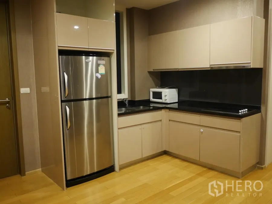 公寓 出租在Watthana, Bangkok - 现代L型厨房，米色橱柜、黑色台面与不锈钢冰箱。
