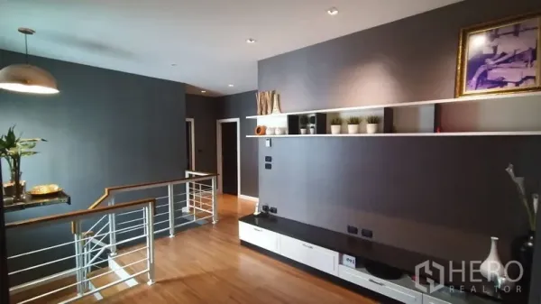 Detached House for sale in Prawet, Bangkok - Upper-floor landing with wood flooring, grey walls, and built-in media shelf beside the staircase.