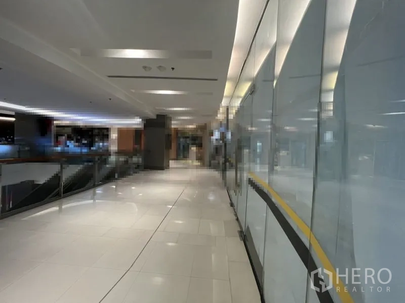 Retail Space for rent in Khlong Toei, Bangkok - Well-lit shopping mall corridor with white tile flooring, glass storefronts, and metal railing.