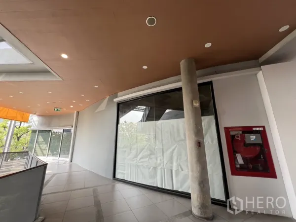 Retail Space for rent in Khlong Toei, Bangkok - Curved corridor outside the unit with floor‑to‑ceiling window and a red fire hose cabinet.