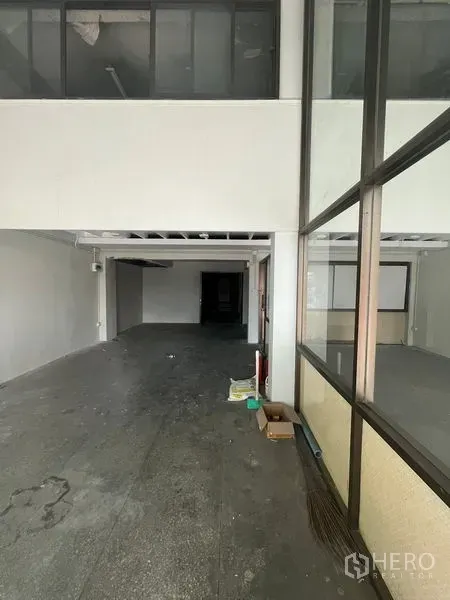 Shophouse for rent in Khlong Toei, Bangkok - Deep open-plan shophouse interior with mezzanine level and glass partitions, concrete floor, and exposed wiring.
