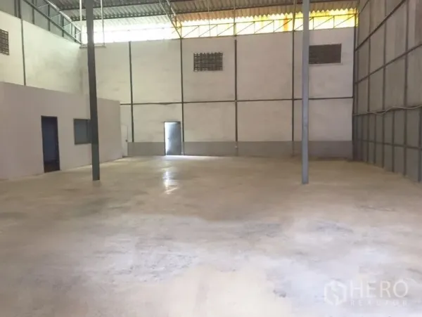 Warehouse for rent in Prawet, Bangkok - Open warehouse floor with steel support columns, ventilation blocks, and a rear access door.