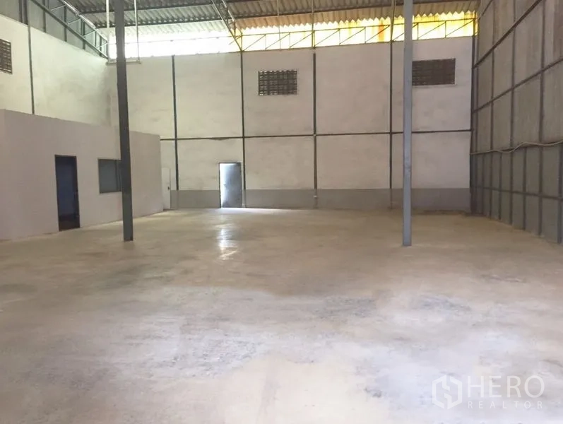 Warehouse for rent in Prawet, Bangkok - Open warehouse floor with steel support columns, ventilation blocks, and a rear access door.