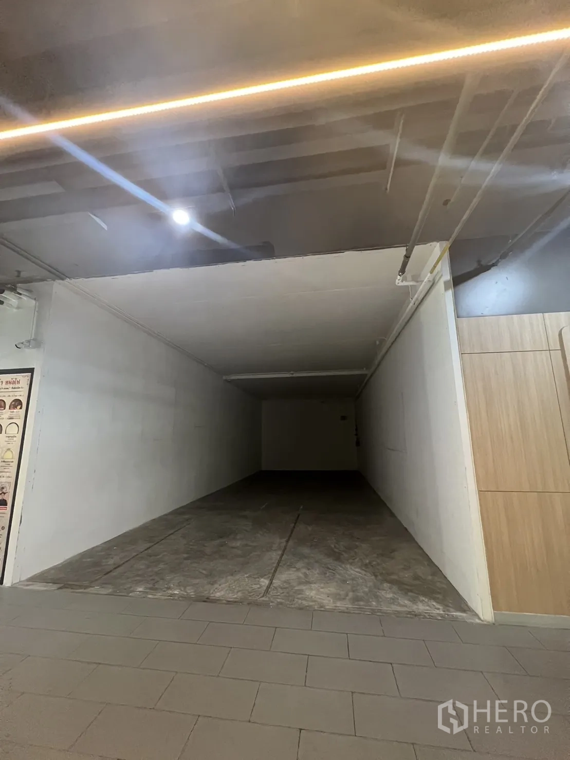Retail Space for rent in Watthana, Bangkok - Empty rectangular retail unit with white walls, concrete floor and exposed ceiling lighting opening to a tiled mall corridor.