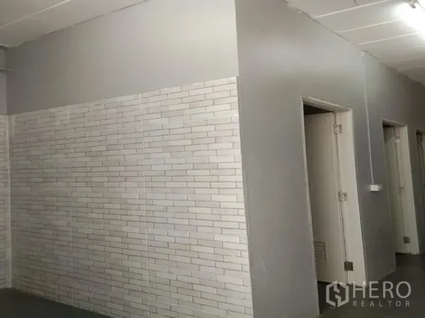 Warehouse for rent in Bang Phli, Samut Prakan - White brick-tile wall section with several doors to restrooms and changing areas inside the warehouse.