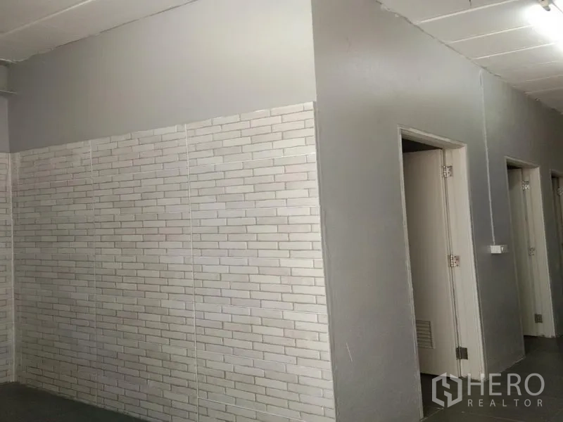 Warehouse for rent in Bang Phli, Samut Prakan - White brick-tile wall section with several doors to restrooms and changing areas inside the warehouse.