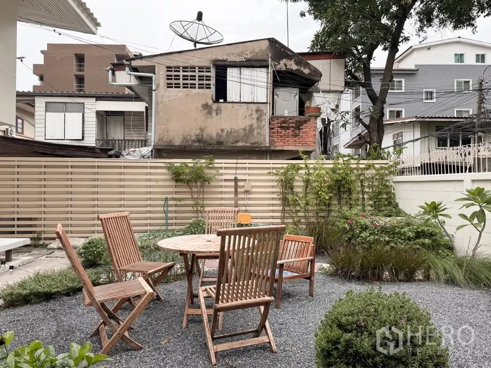 Detached House for rent in Huai Khwang, Bangkok - Private gravel patio with wooden outdoor dining set and green shrubs.