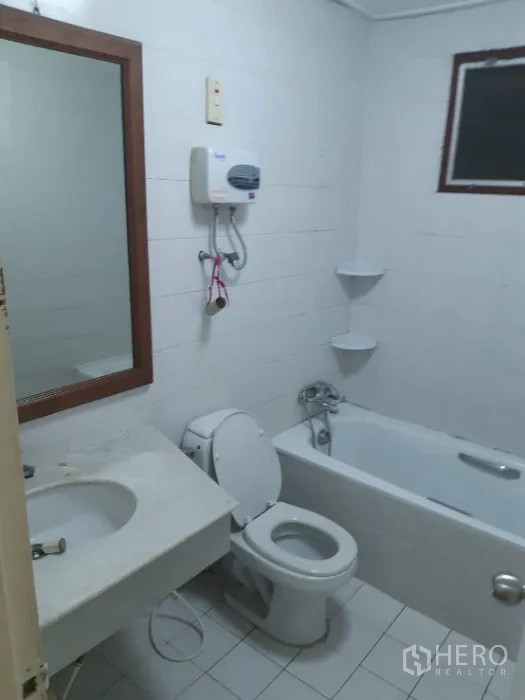 Townhouse for rent in Khlong Toei, Bangkok - White tiled bathroom with bathtub, toilet, vanity and water heater.