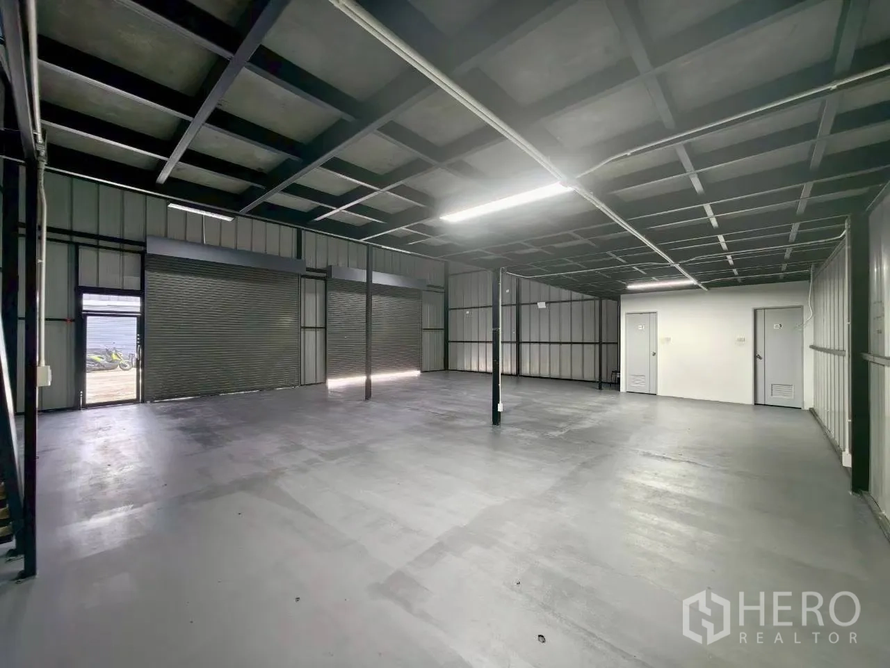 Warehouse for rent in Suan Luang, Bangkok - Wide warehouse bay with closed shutters, bright strip lighting, and a white service core.