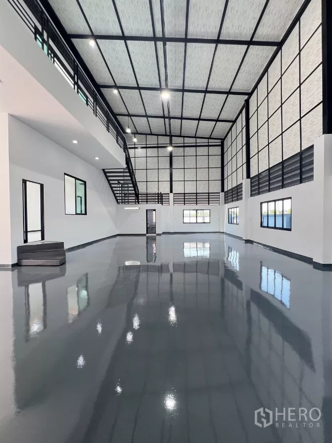 Warehouse for sale in Lam Luk Ka, Pathum Thani - Open industrial hall with black steel trusses, mezzanine and reflective epoxy floor.