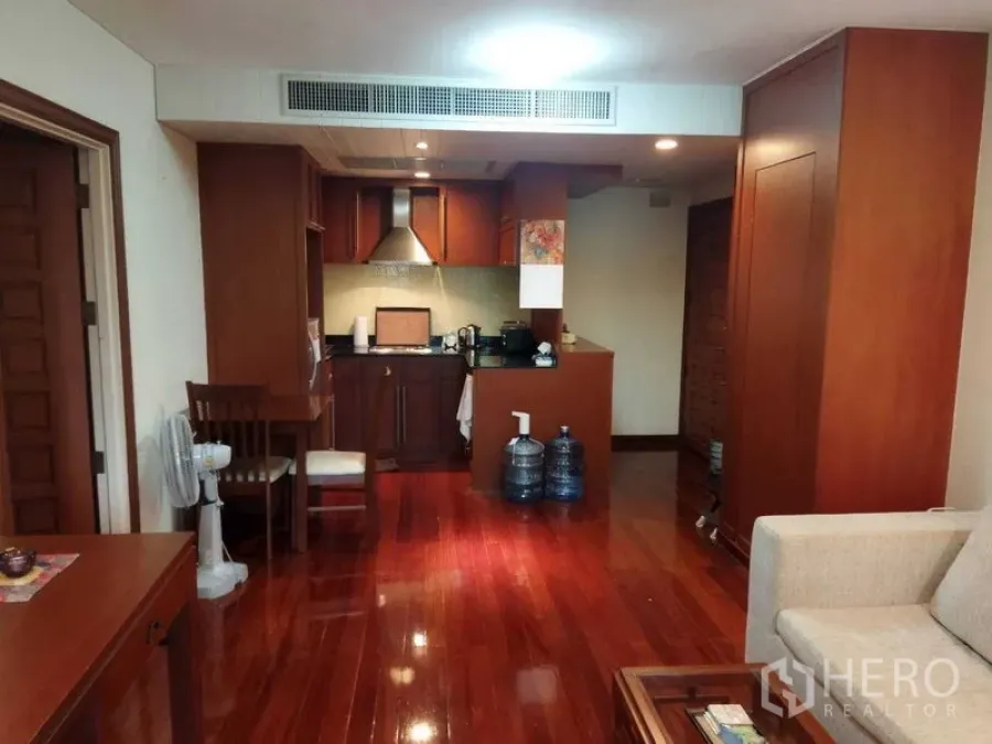 Condominium for rent in Pathum Wan, Bangkok - Open‑plan living area with polished wood floors and a compact kitchenette with range hood.