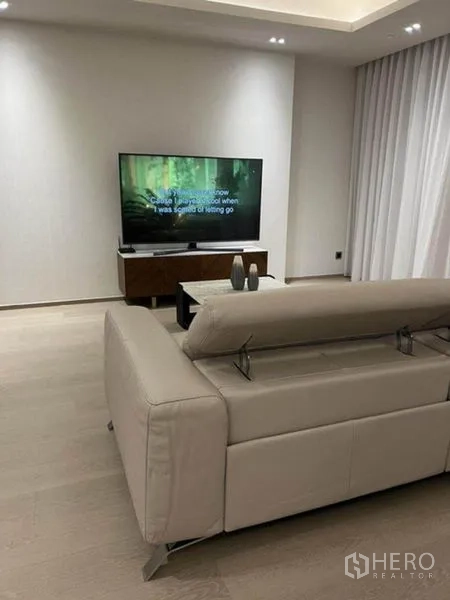 Condominium for rent in Pathum Wan, Bangkok - Cozy living corner with beige leather sofa facing the TV and sheer drapes.