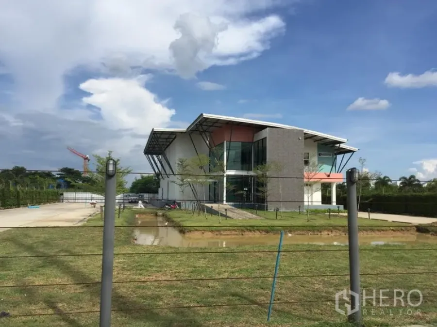 Factory for rent in Lam Luk Ka, Pathum Thani - Modern factory with glass-fronted office, landscaped lawn, driveway and pond in Lam Luk Ka, Pathum Thani under blue sky.
