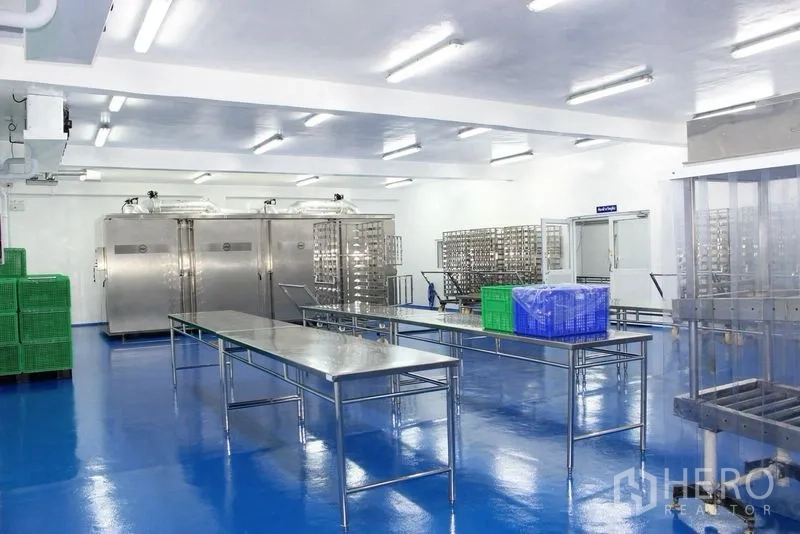 Factory for rent or sale in Krathum Baen, Samut Sakhon - Bright factory room with stainless tables, wheeled racks, and suspended utilities.