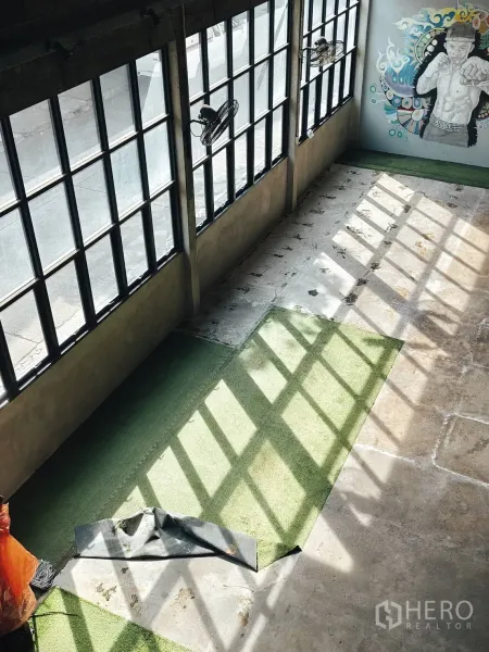 Warehouse for rent in Khlong Toei, Bangkok - Sunlit warehouse interior with tall grid windows, concrete floor, a green turf strip and a colorful wall mural.