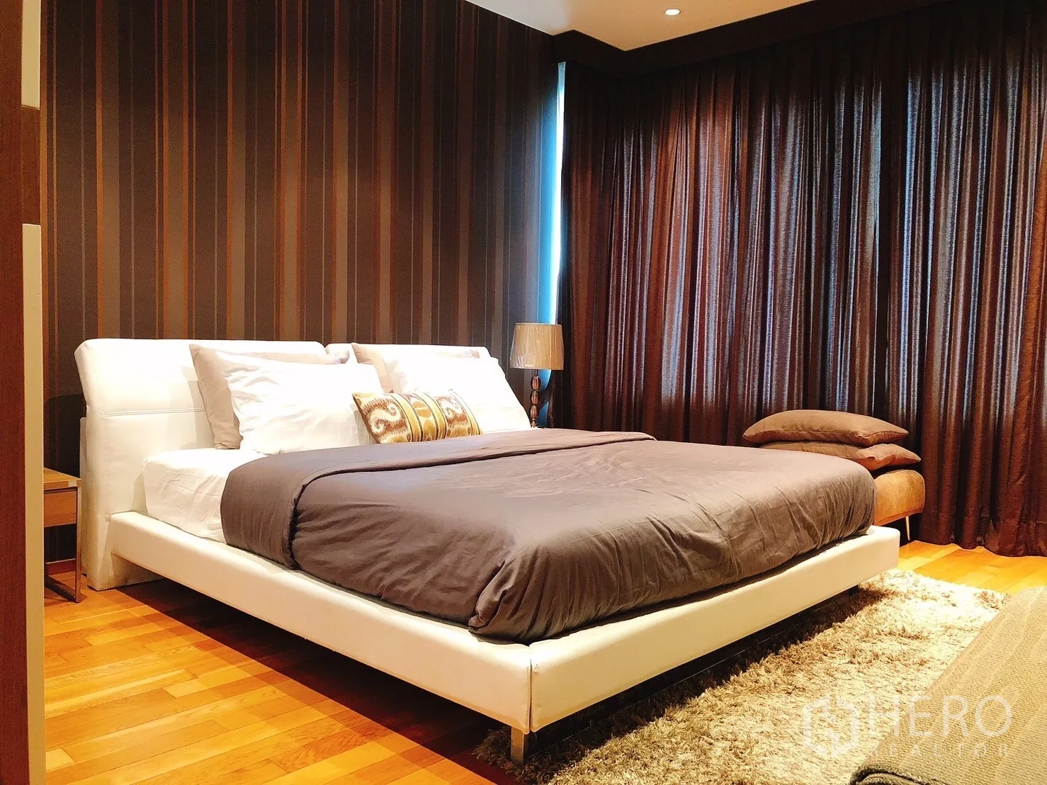 Condominium for rent in Khlong Toei, Bangkok - Cozy bedroom with white platform bed, dark curtains and wood flooring.