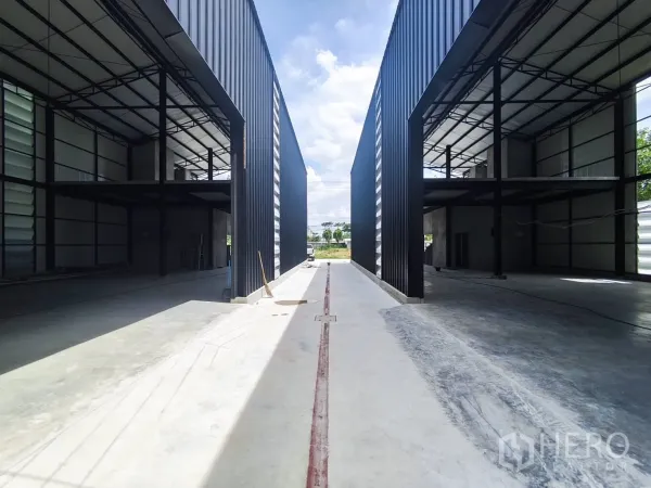 Warehouse for rent in Sai Mai, Bangkok - Two warehouse bays facing a central access lane with high roofs and open interiors.