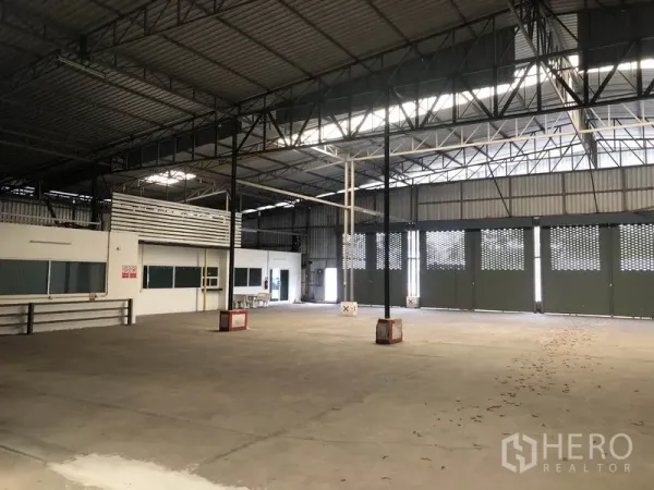 Warehouse for rent in Pak Kret, Nonthaburi - Warehouse floor with several ventilated roller doors, sturdy concrete surface, and adjacent office block.