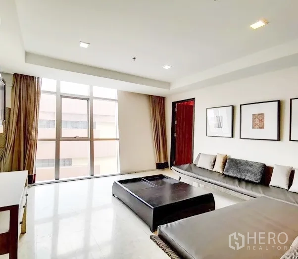 Condominium for rent in Khlong Toei, Bangkok - Bright living room with floor‑to‑ceiling windows, long built‑in sofa and a low coffee table.