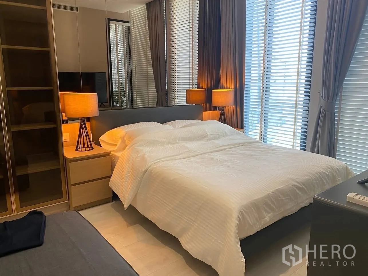 Condominium for rent in Pathum Wan, Bangkok - Bright bedroom with floor-to-ceiling windows, blinds, and matching bedside lamps.