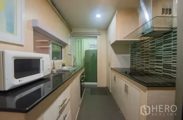 Townhouse for rent in Suan Luang, Bangkok - Galley kitchen featuring light wood cabinetry, black stone countertops, cooktop and range hood.