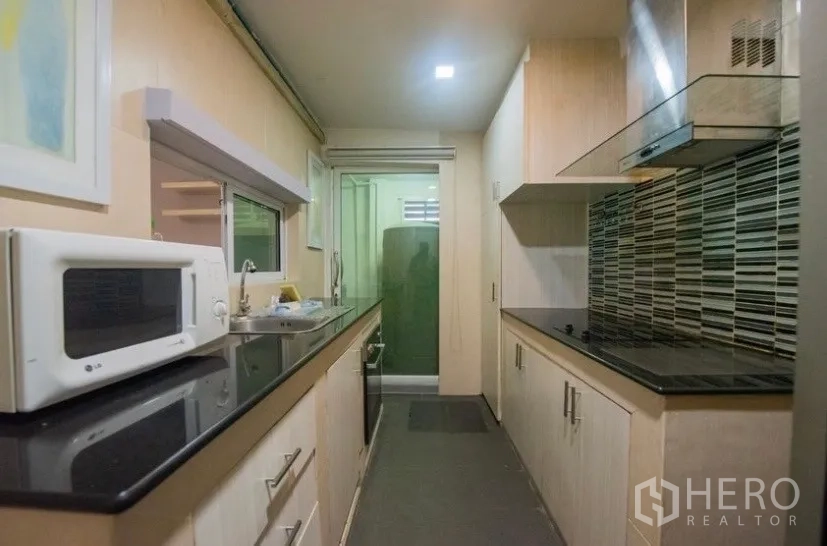Townhouse for rent in Suan Luang, Bangkok - Galley kitchen featuring light wood cabinetry, black stone countertops, cooktop and range hood.