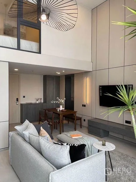 Condominium for rent in Pathum Wan, Bangkok - Loft-style condo with mezzanine bedroom behind glass, statement pendant light, dining set and a tall, bright ceiling.