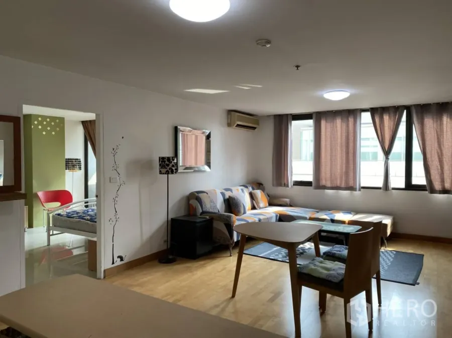 Condominium for rent in Pathum Wan, Bangkok - Bright open-plan living room with wood floors, L-shaped sofa, dining table and doorway to the bedroom.