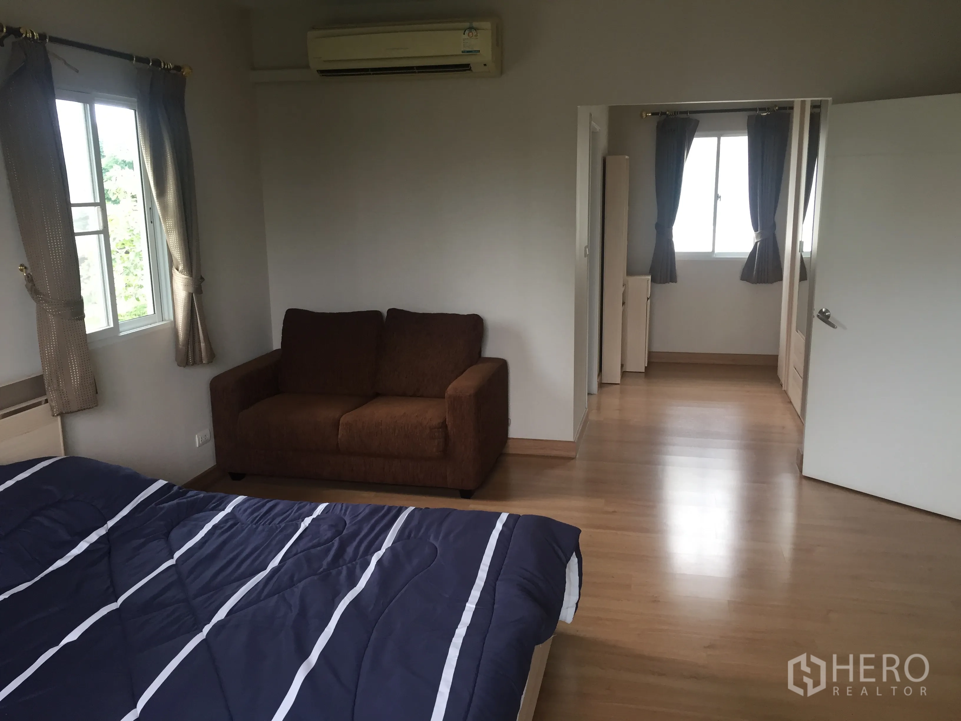 Detached House for rent in Pathum Thani - Bedroom with brown sofa, air conditioner, several windows and access to a dressing area.