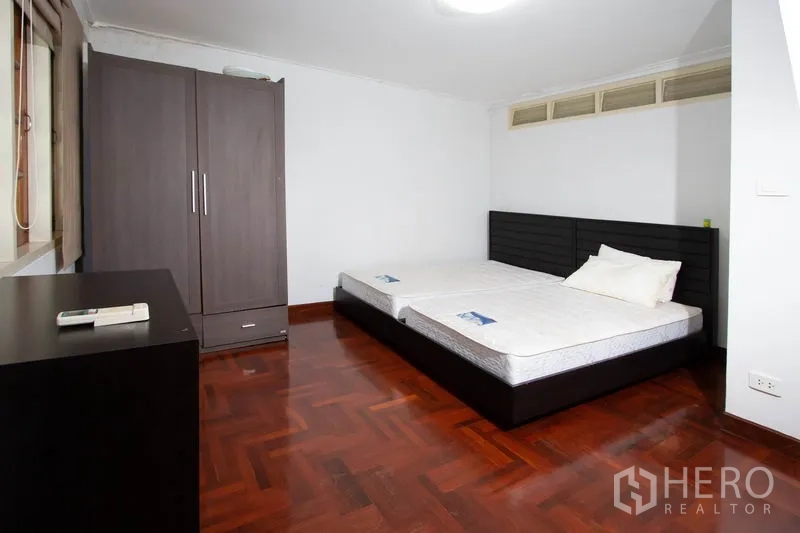 Townhouse for rent in Khlong Toei, Bangkok - Secondary bedroom with wardrobe, large bed base and parquet flooring.