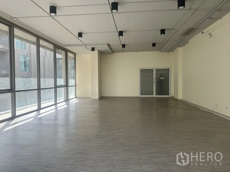Office Space for rent in Phra Khanong, Bangkok - Spacious office interior with a long window wall, tiled flooring, and double glass entry doors.