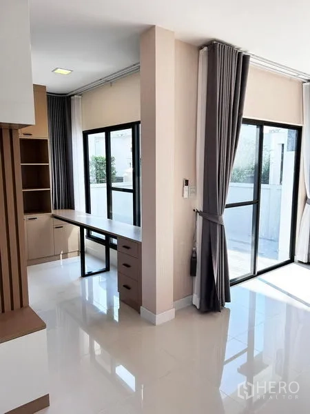 Detached House for rent or sale in Prawet, Bangkok - Ground-floor area with sliding glass doors, long desk, and curtains.