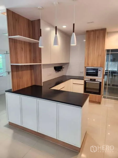 Detached House for rent in Sathon, Bangkok - U-shaped kitchen with white cabinets, black countertops, and pendant lights.