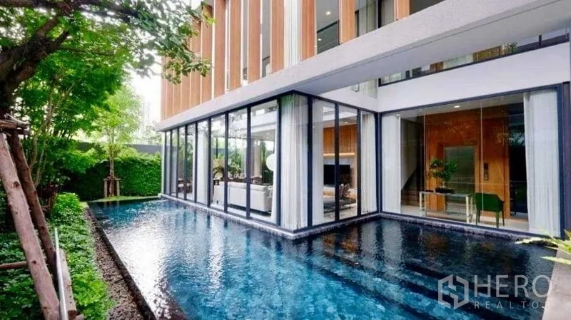 Detached House for sale in Huai Khwang, Bangkok - L-shaped swimming pool wrapping the glass living room with sliding doors.