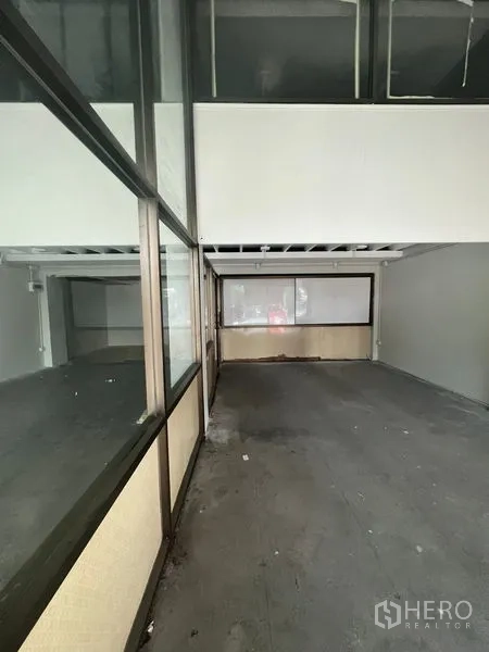Shophouse for rent in Khlong Toei, Bangkok - Long corridor-style commercial space beside framed glass walls under a mezzanine ceiling.