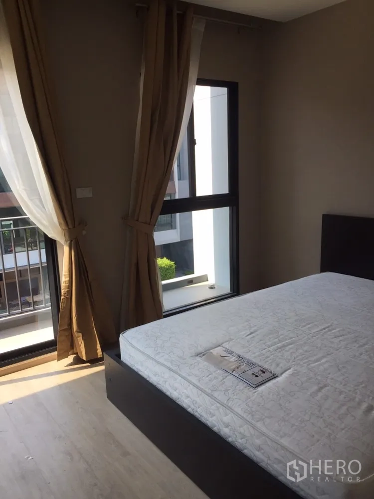 Townhouse for rent in Suan Luang, Bangkok - Cozy bedroom with large windows, curtains, and a double bed frame.
