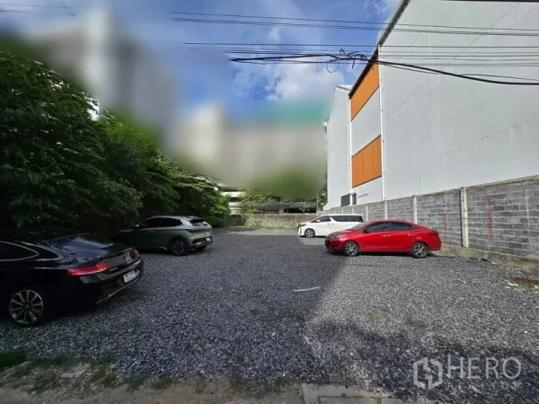 Home Office for rent in Chatuchak, Bangkok - Gravel parking area with several cars beside a low-rise building and trees in Chatuchak, Bangkok.