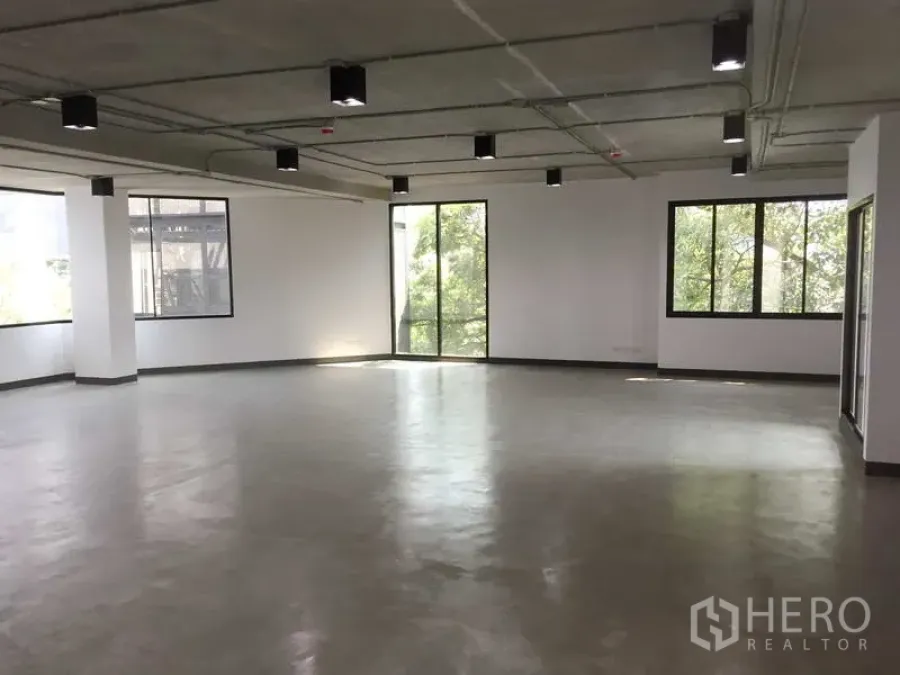 Office Space for rent in Khlong Toei, Bangkok - Open-plan 122 sqm office with large windows, polished concrete floor, exposed ceiling lights and leafy views near BTS Thong Lo.