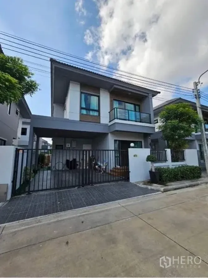 บ้าน ขายในKhan Na Yao, Bangkok - ด้านหน้าบ้านเดี่ยวสองชั้นสไตล์โมเดิร์น มีกำแพงรั้วและที่จอดรถในบ้านพร้อมระเบียง