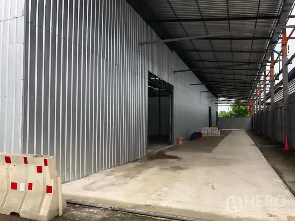 Warehouse for rent in Pak Kret, Nonthaburi - Covered side driveway along corrugated metal exterior for truck access and loading.