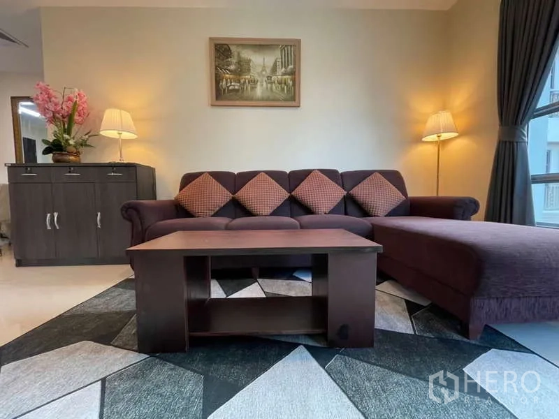 Apartment for rent in Khlong Toei, Bangkok - Living room with L-shaped sofa, patterned rug and coffee table.