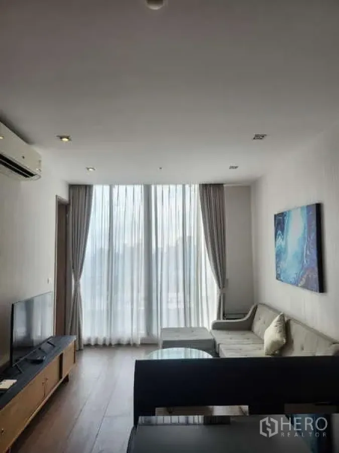 Condominium for rent in Khlong Toei, Bangkok - Another angle of the bright living room showing sectional sofa, TV and tall curtains.