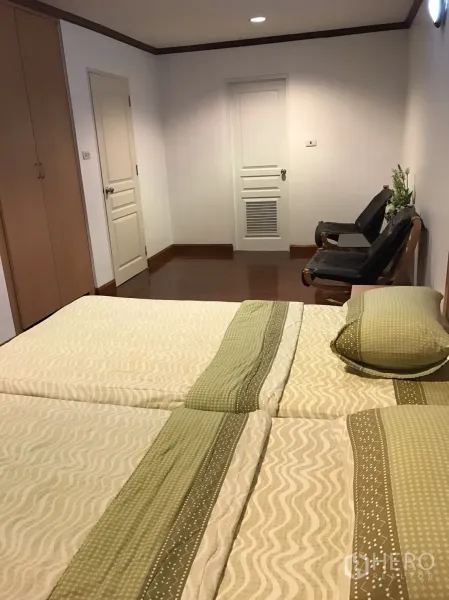 Condominium for rent in Khlong Toei, Bangkok - Bright twin bedroom with wardrobes, white doors and seating area.