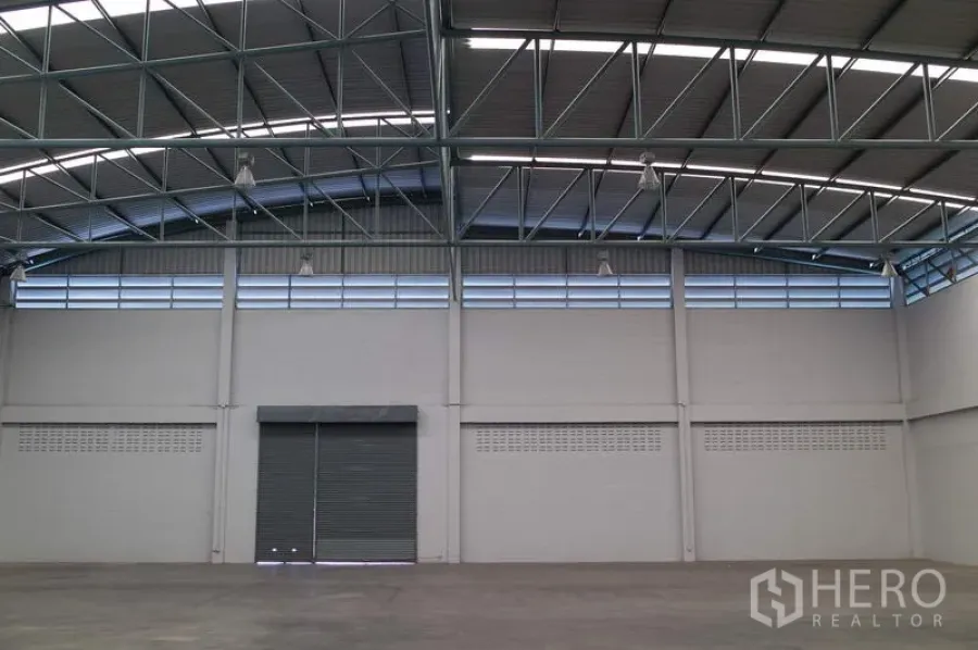 工厂 出租在Pathum Thani - 高挑厂房仓库内景，钢结构屋顶、上部通风窗与大型卷闸门。