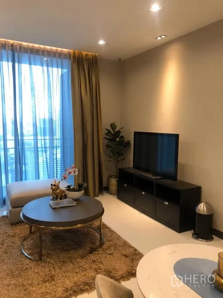 Condominium for rent in Khlong Toei, Bangkok - Living area with TV console, balcony access and a round coffee table on a plush rug.