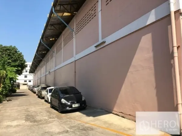 Warehouse for rent in Sam Phran, Nakhon Pathom - Side elevation of the warehouse showing covered eaves, concrete driveway and a row of parking spaces.