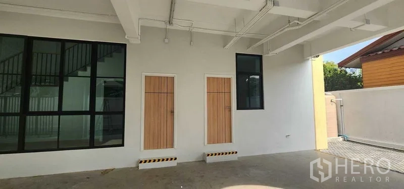 带办公室的家 出租在Bang Kapi, Bangkok - 一层有顶停车区，配两扇木门与黑框窗户。